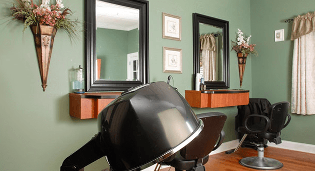 A cozy salon interior featuring mirrors and hair drying stations against green walls.