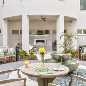 A beautifully decorated outdoor patio area with a round table, chairs, and a garden fountain.