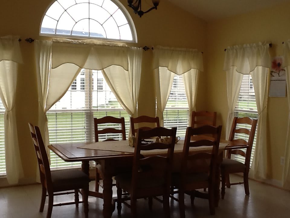 A cozy dining room with a wooden table, several chairs, and large windows with curtains.