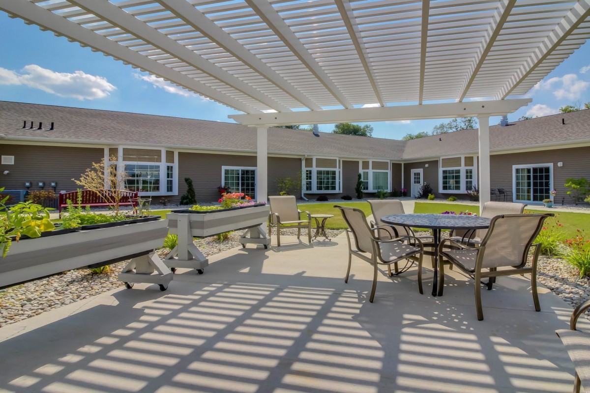 A sunny outdoor patio with a pergola, featuring tables and chairs for seating.