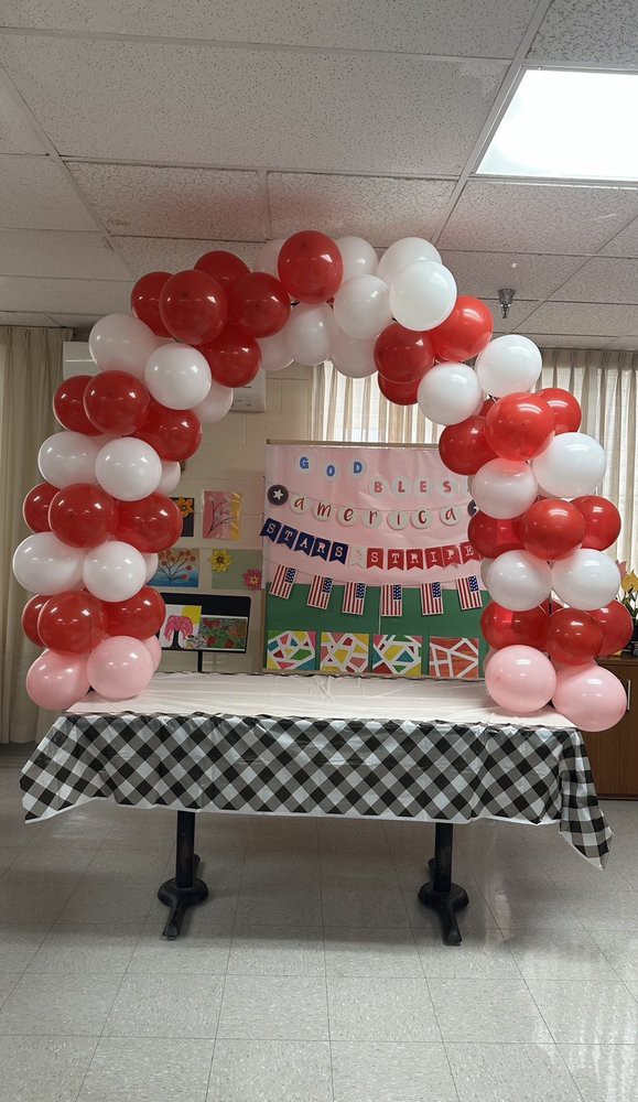 A festive balloon arch made of red and white balloons adorns an indoor party setting with a checkered tablecloth.