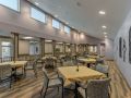 A spacious dining area with multiple tables and chairs, featuring modern lighting and high windows.