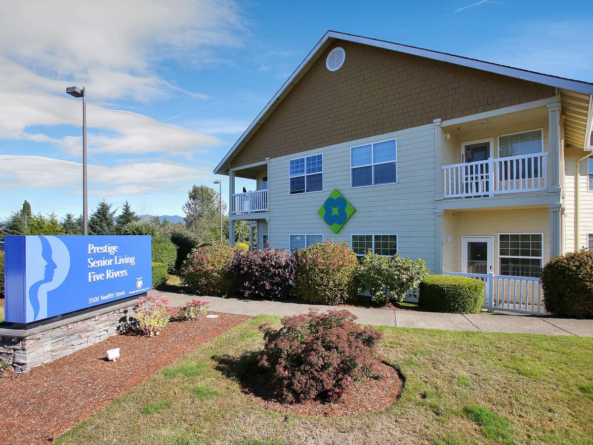 A two-story building with a surrounding landscape, featuring a blue sign and clear sky.