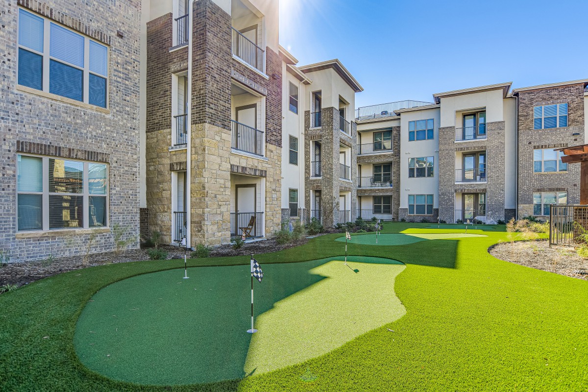 An apartment complex featuring a landscaped outdoor area with a putting green on a sunny day.