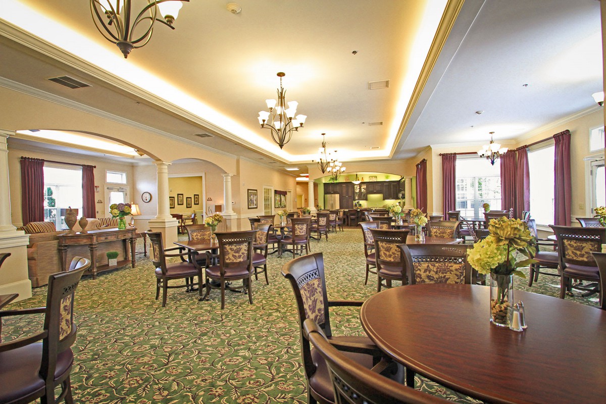 A spacious and elegantly decorated dining area with tables and chairs, featuring chandeliers and a carpeted floor.