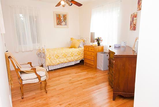 A cozy bedroom with wooden floors, featuring a single bed adorned with yellow bedding and decorative pillows.