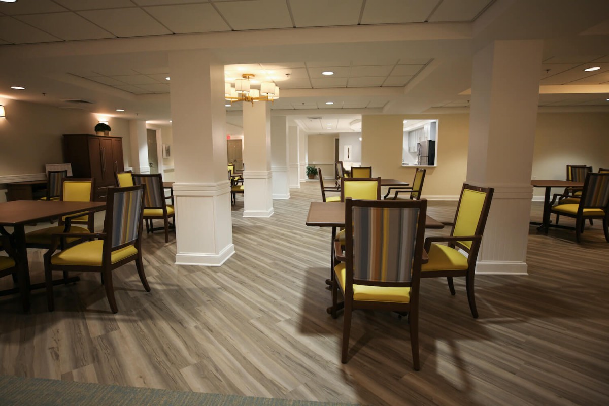 An elegantly designed dining area with wooden tables and vibrant yellow upholstered chairs, set against a backdrop of columns and warm lighting.