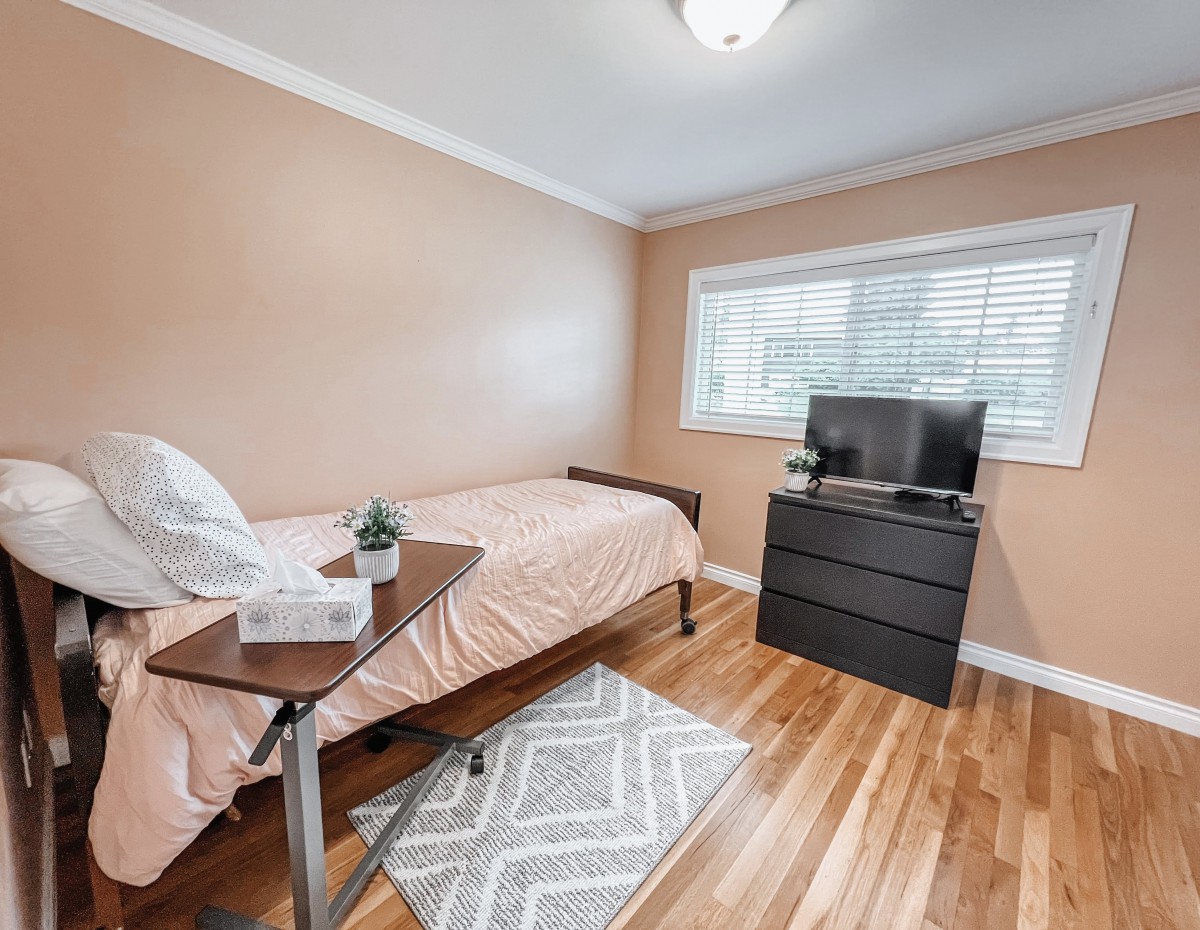 A minimalist bedroom with a single bed, dresser, and window, featuring neutral tones and hardwood flooring.