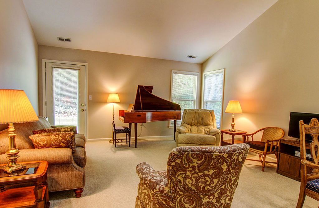 A cozy living room with a grand piano, comfortable chairs, and warm lighting.