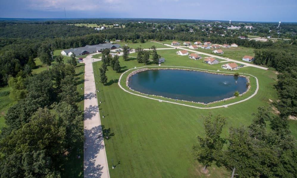 A scenic aerial view of a grassy park featuring a large pond and surrounding residential areas.