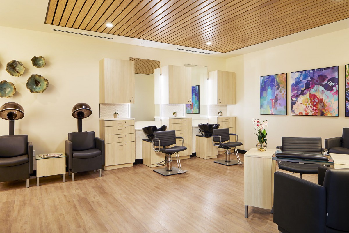 A modern hair salon with stylish chairs and mirrors, featuring wooden ceilings and contemporary artwork.