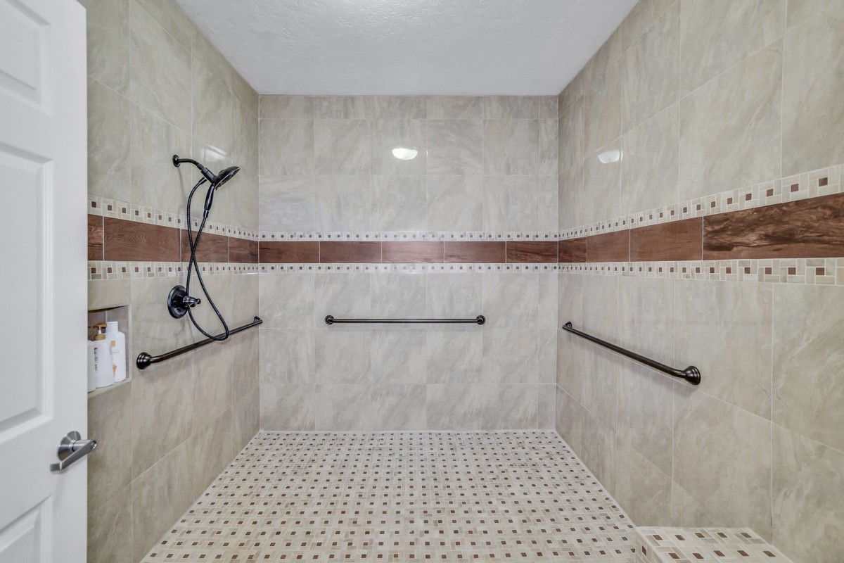 A modern walk-in shower with tiled walls and floor, featuring grab bars for safety.