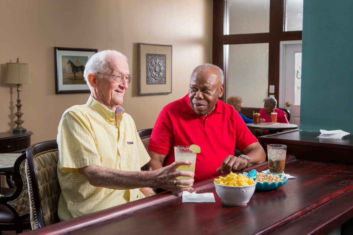 Two senior men enjoying a conversation over drinks and snacks at a bar.