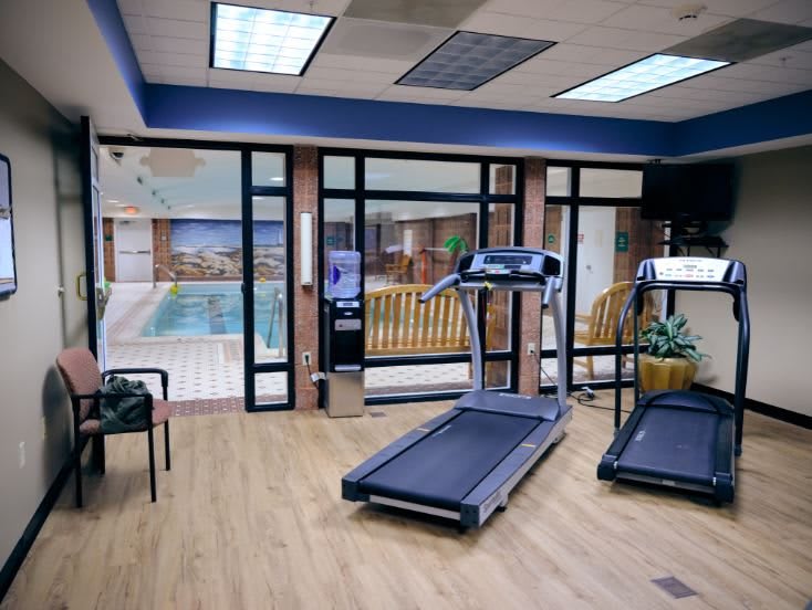 A modern fitness room featuring treadmills and an indoor pool area in the background.