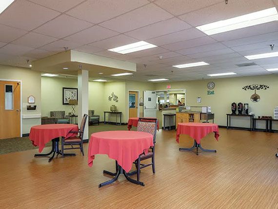 A well-lit cafeteria with round tables covered in red tablecloths, providing a welcoming community dining area.