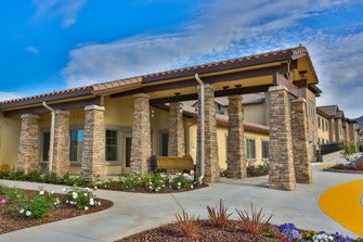 A modern building entrance with stone columns and landscaped surroundings under a clear blue sky.