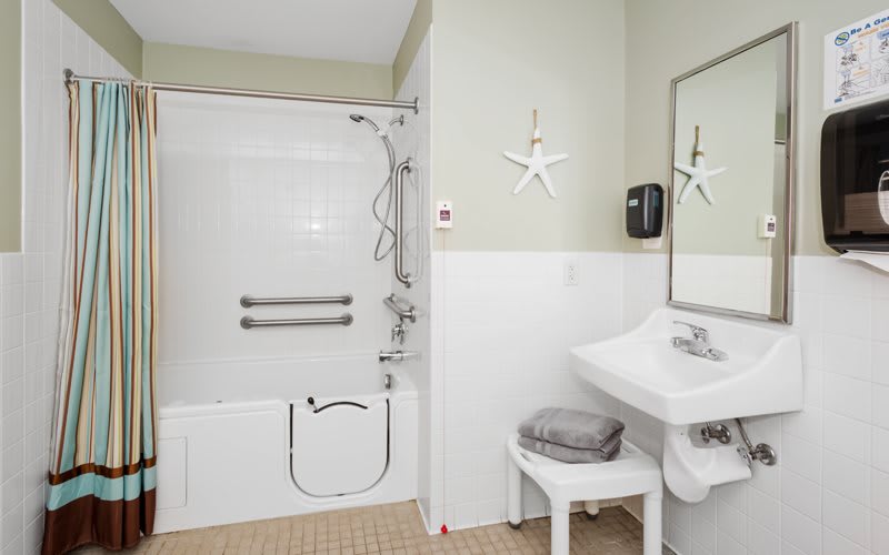 An accessible bathroom with a bathtub featuring support bars, a sink with a towel on a stool, and starfish-themed wall decor.