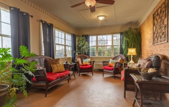 A cozy living room with wicker furniture, bright red cushions, and large windows allowing natural light to flood the space.