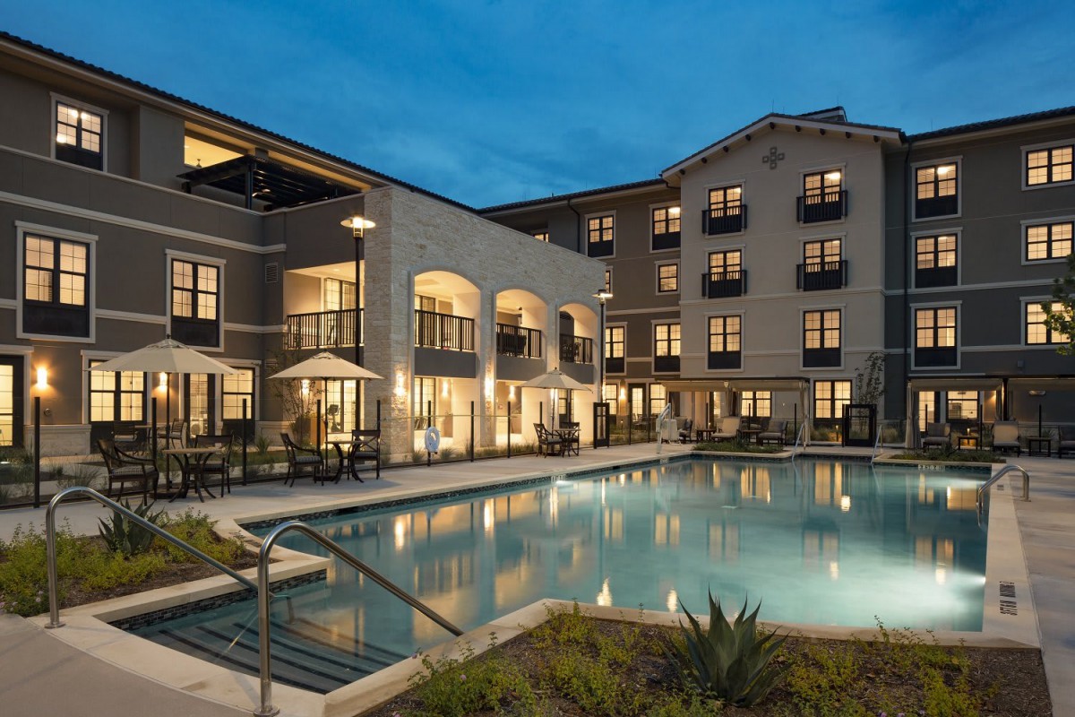 A luxurious apartment complex with a well-lit swimming pool at dusk.