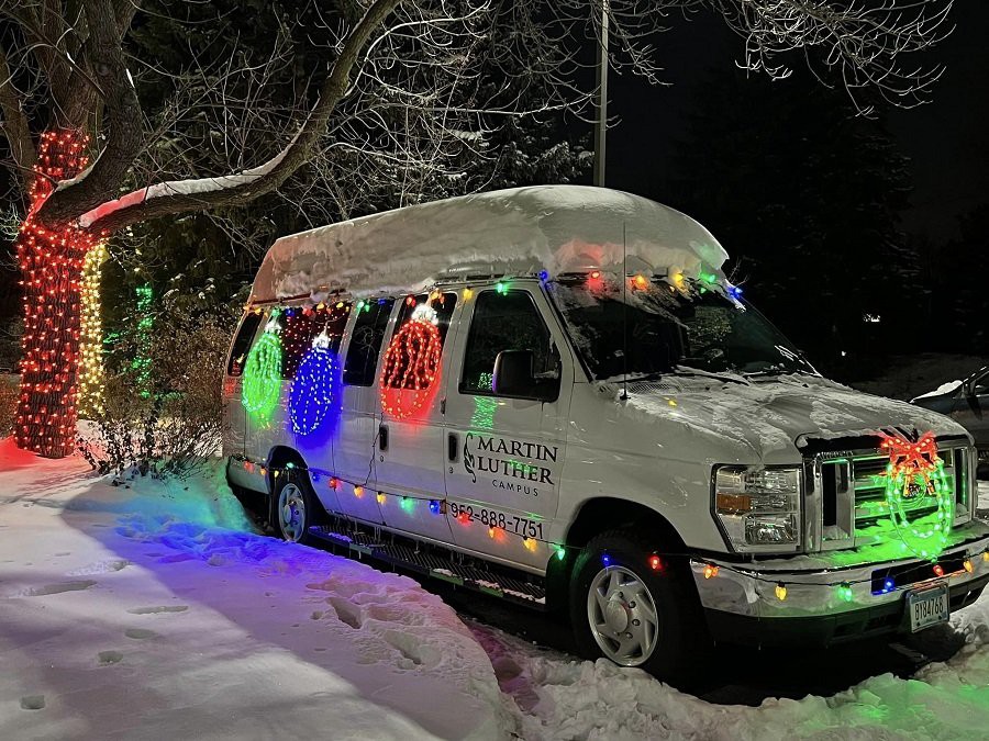 A van decorated with colorful Christmas lights parked in a snowy area at night.