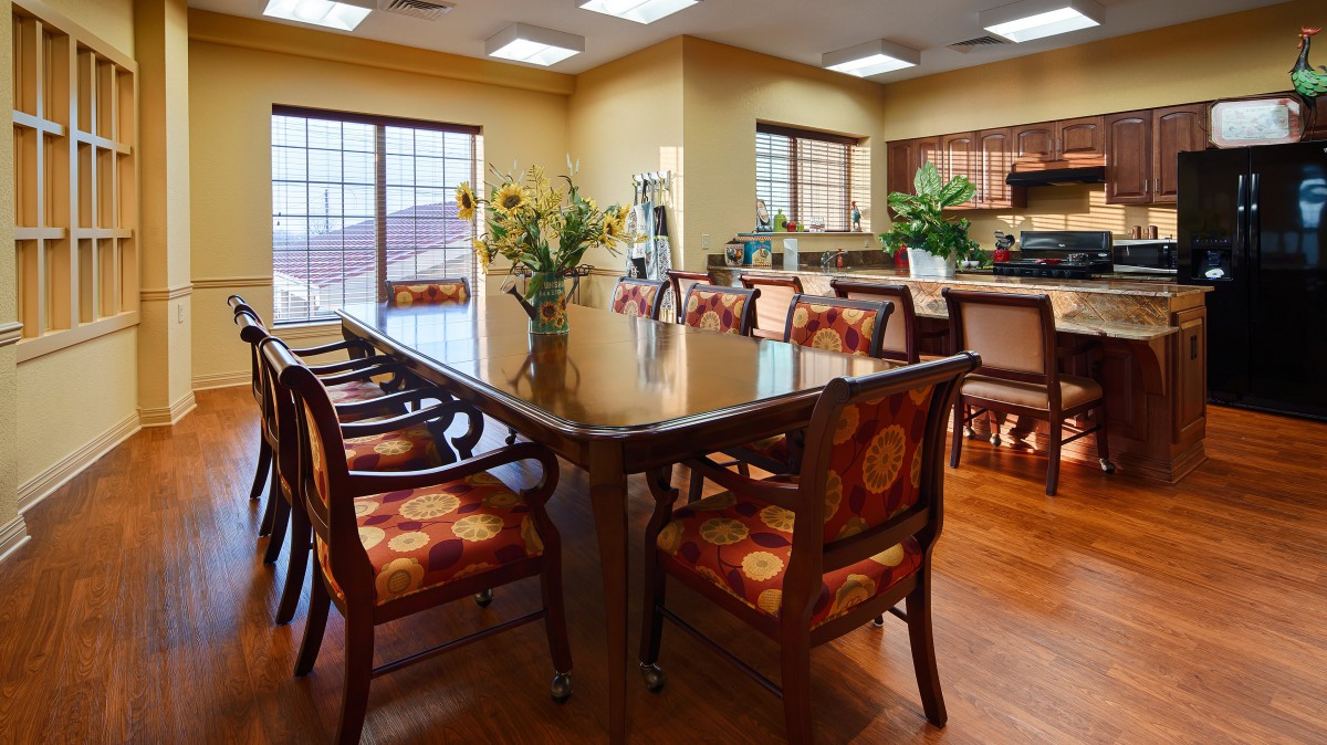 A well-lit dining room with a large table and upholstered chairs surrounded by windows.