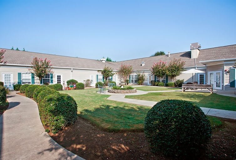 A well-maintained courtyard with manicured bushes and a central garden area in front of a single-story building.