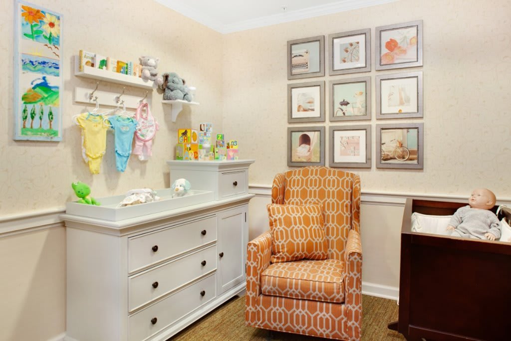 A cozy nursery featuring a changing table, an upholstered rocking chair, and decorative wall art.