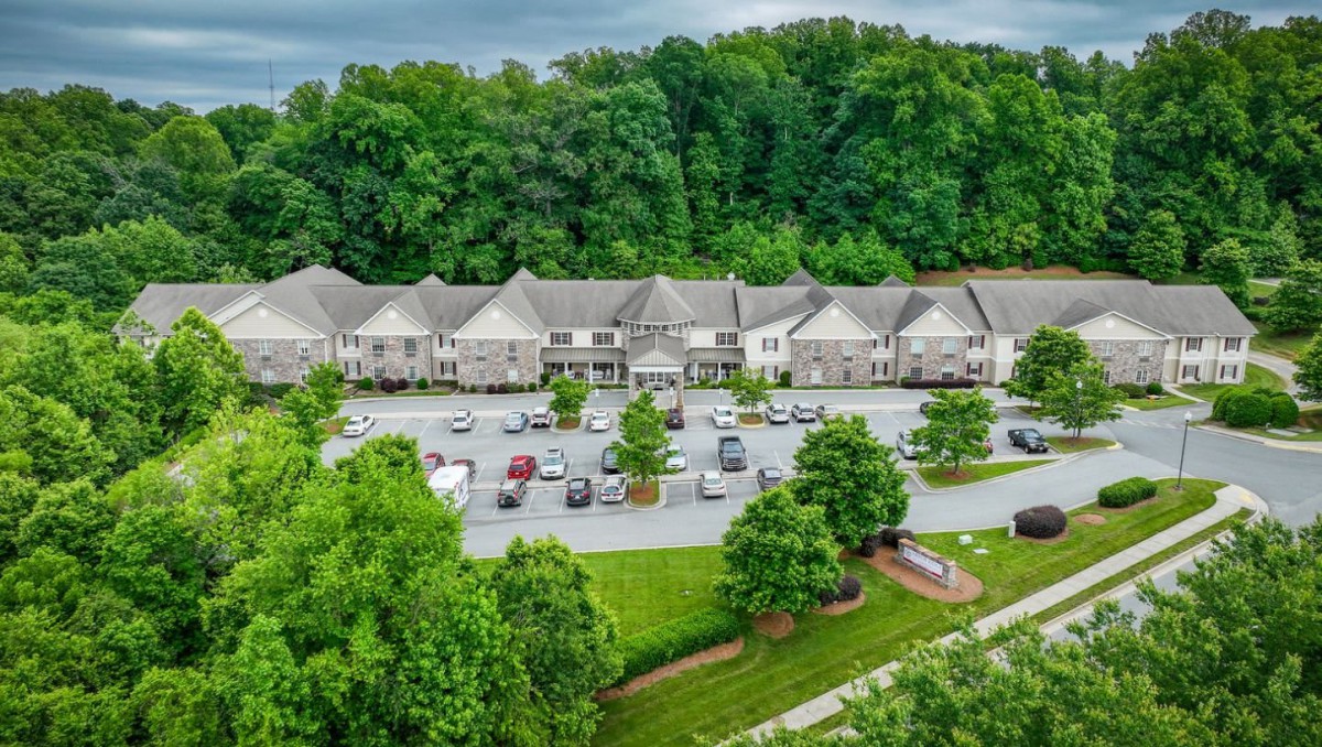 Aerial view of a residential complex surrounded by lush greenery and a parking lot.