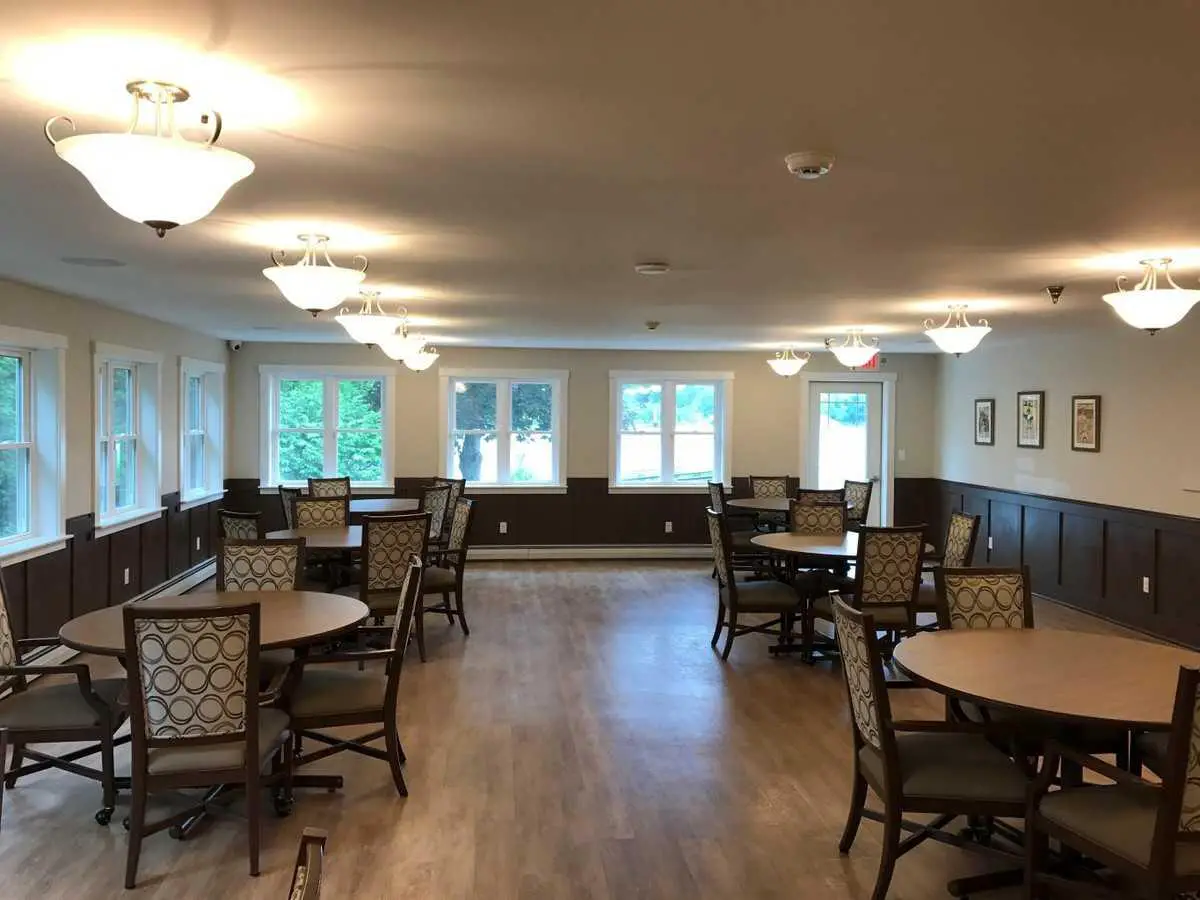 A spacious dining room with multiple tables and chairs, featuring warm lighting and large windows.