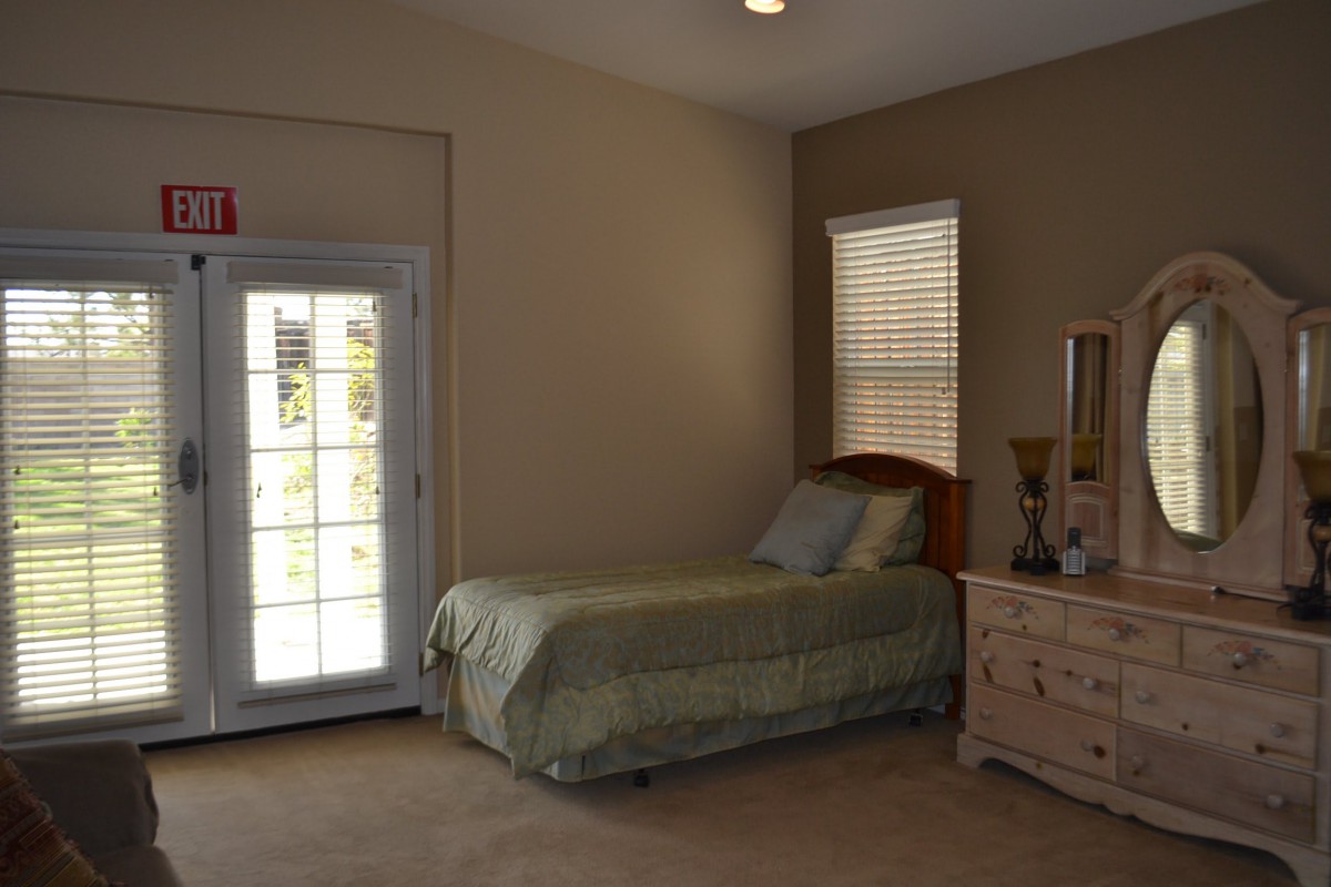 A cozy bedroom with a single bed, dresser, and mirror, featuring a window and a door leading outside.
