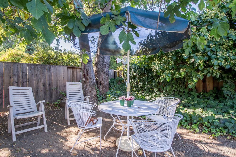 A peaceful garden patio with white metal furniture and a shaded umbrella.