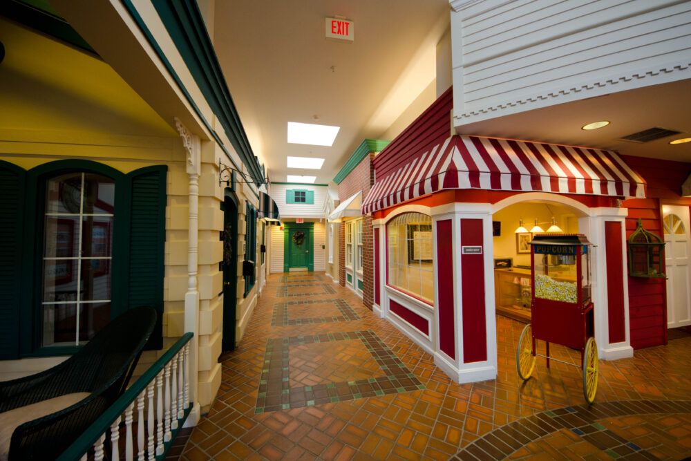 A vintage-style indoor hallway featuring storefronts with red and white awnings.