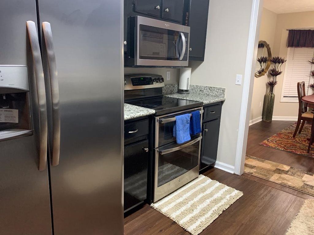 A modern kitchen featuring stainless steel appliances and a cozy rug on hardwood flooring.