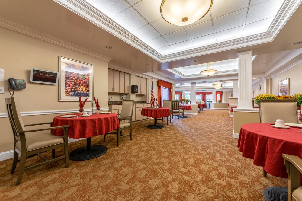 A spacious dining room with tables and chairs, adorned with red tablecloths and modern lighting.
