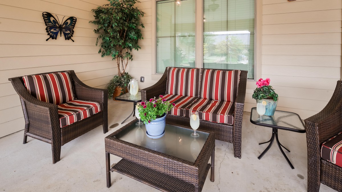 A cozy outdoor patio setup with wicker furniture, striped cushions, and decorative plants.