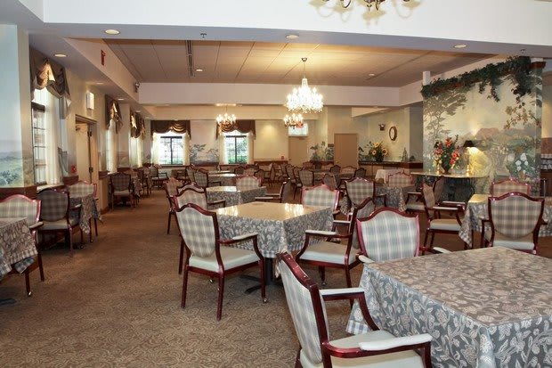 An elegant dining room featuring multiple tables and chairs, lit by chandeliers.