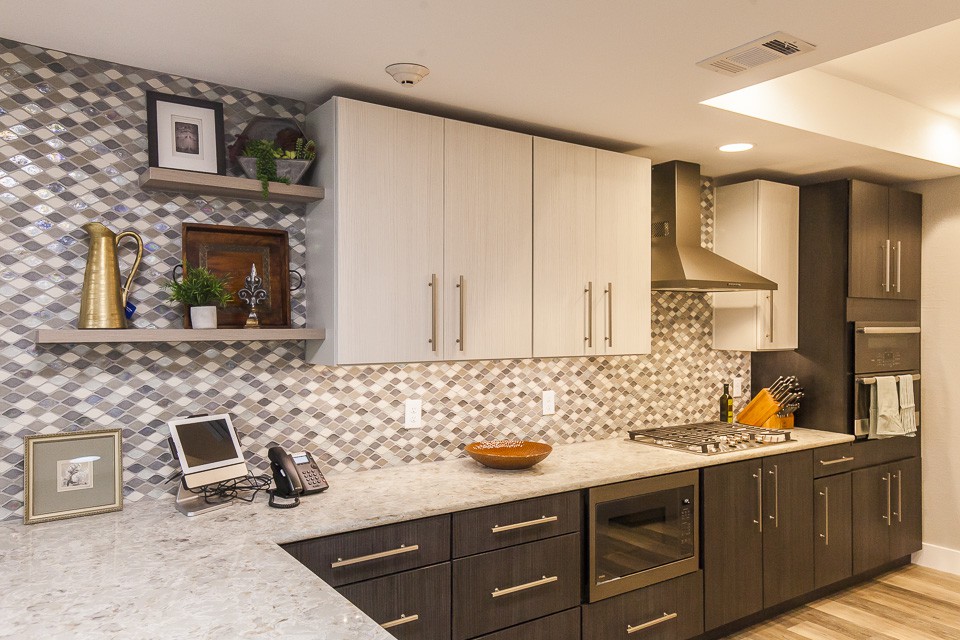 A modern kitchen featuring white upper cabinets, dark lower cabinets, and a stylish mosaic backsplash with stainless steel appliances.