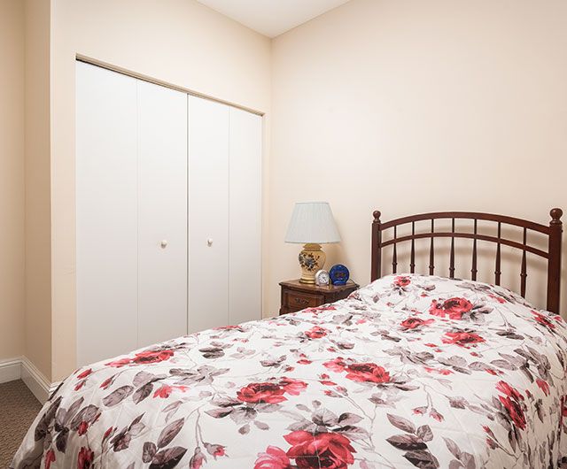A cozy bedroom featuring a bed with floral bedding, a nightstand with a lamp, and a closed closet.