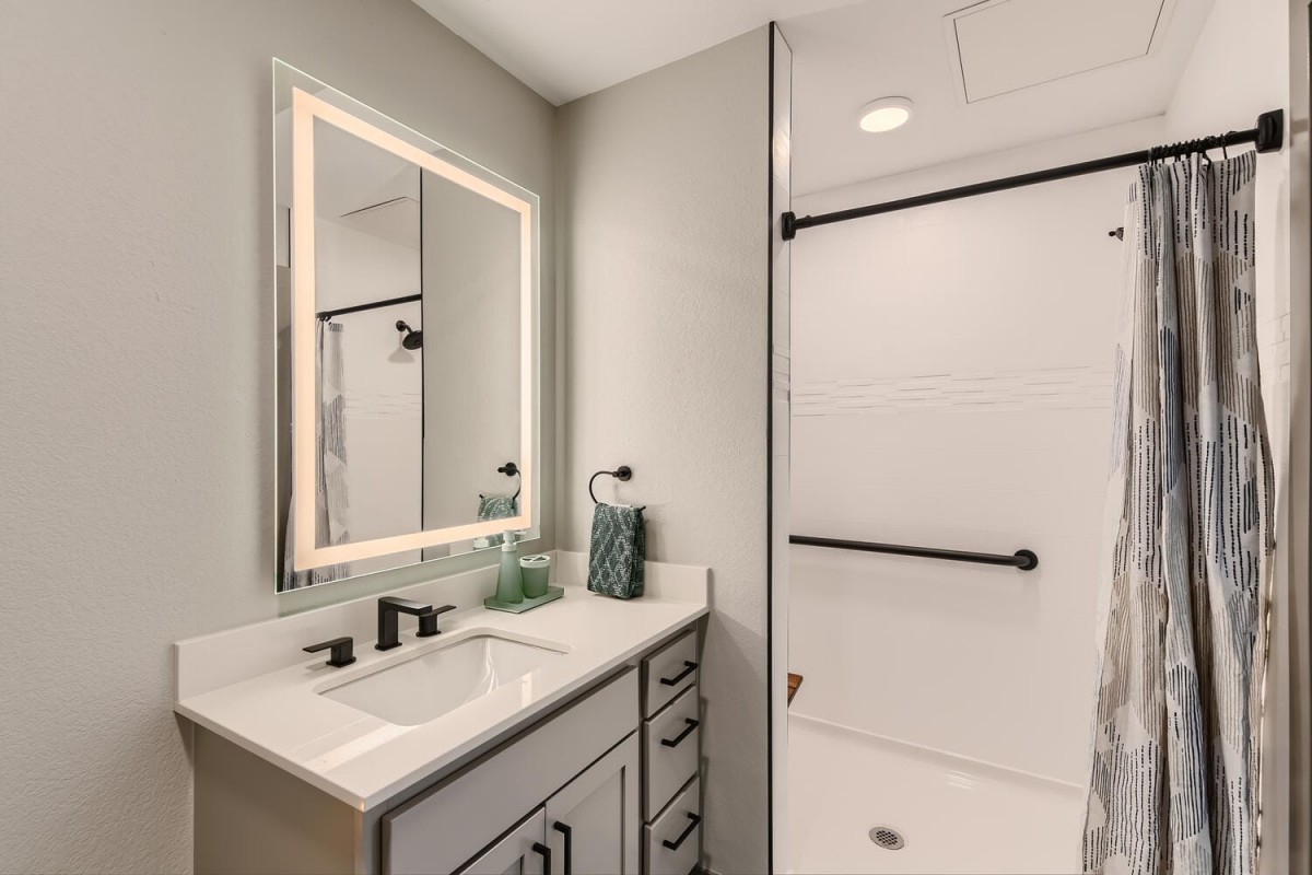 A modern bathroom featuring a sleek sink and illuminated mirror alongside a walk-in shower.