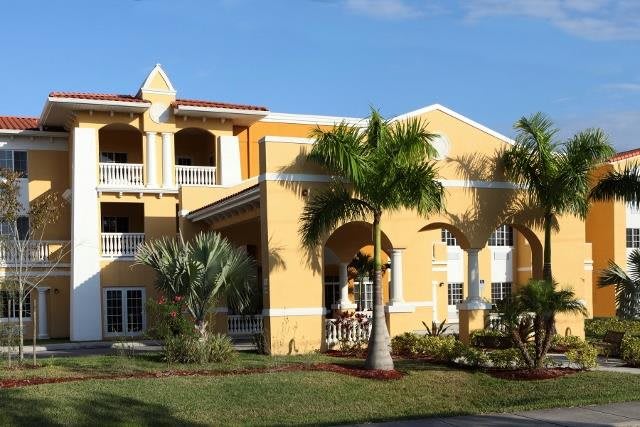 A tropical-style yellow house surrounded by palm trees and lush landscaping.