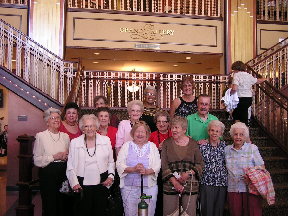 A group of elderly women smiling together in front of a staircase.