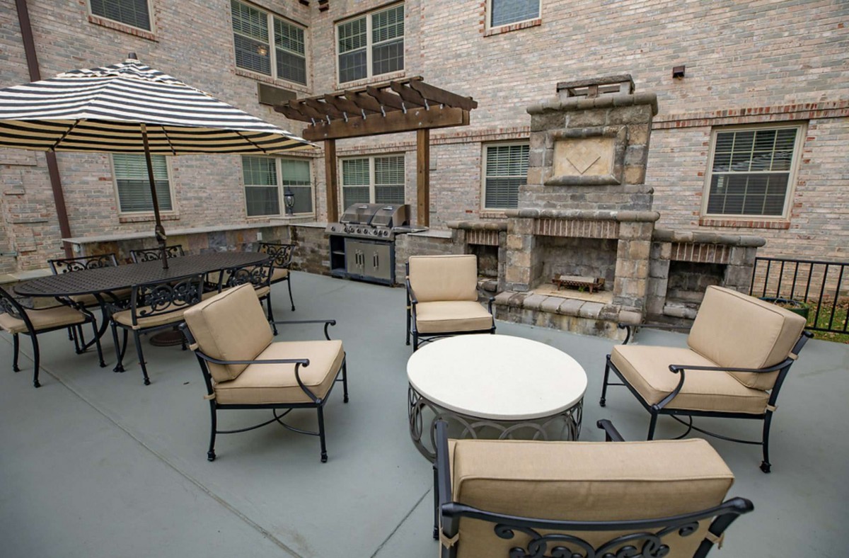 An outdoor patio with a seating area, featuring cushioned chairs, a round table, and a built-in fireplace.