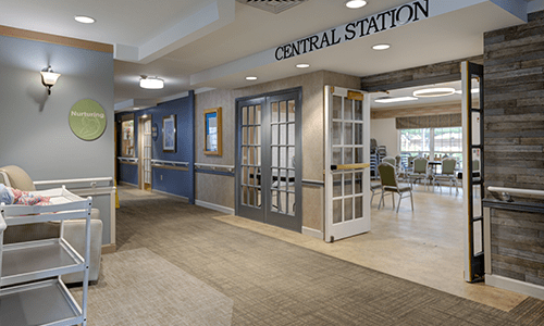 A well-decorated hallway leads to a central station area with glass doors and seating.