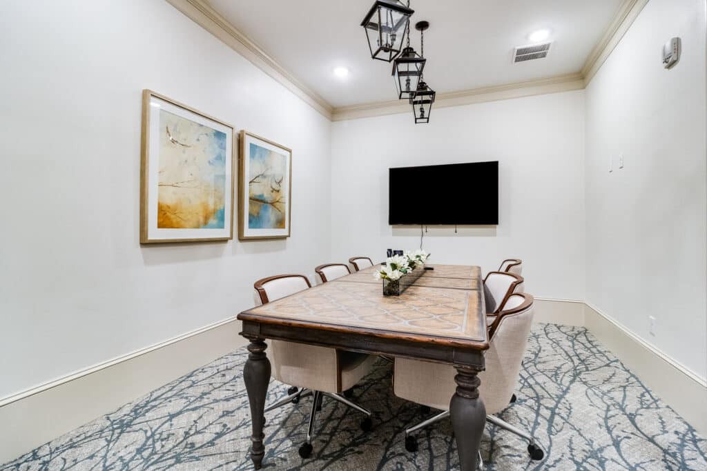 A modern conference room featuring a large wooden meeting table, elegant chairs, and minimalist decor with wall art and hanging lights.