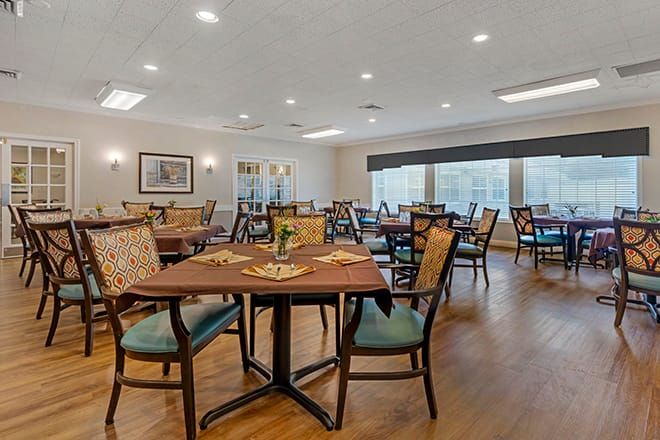 A spacious dining area with neatly arranged tables and chairs, featuring warm lighting and a wooden floor.