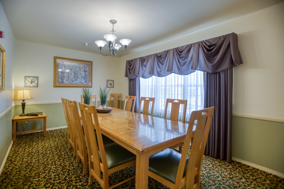 A dining room with a large wooden table, surrounded by chairs and lit by a chandelier.