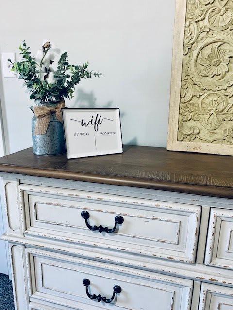 A rustic wooden dresser with a vase of greenery and a decorative sign.