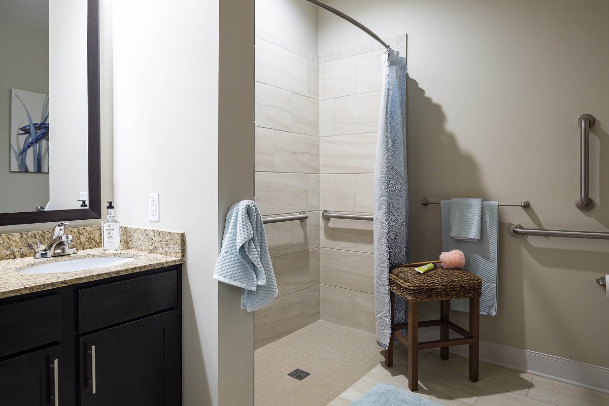 A modern bathroom featuring a walk-in shower with blue towels and a small wooden stool.