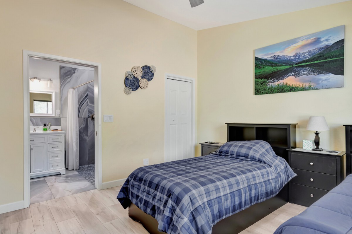 A bedroom with a blue plaid bedspread, wall art, and an open doorway leading to another room.