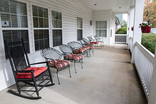 A spacious porch with multiple chairs lined up along the wall, including a rocking chair.